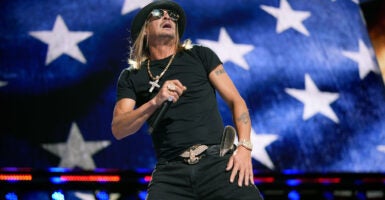 Kid Rock performs at Republican National Convention in front of large screen of American flag.