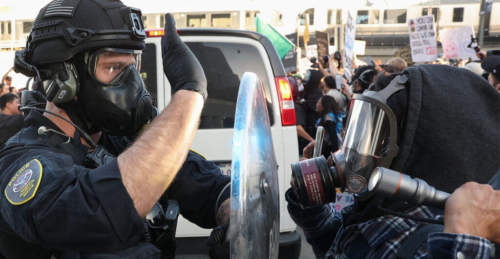 A US Department of Homeland Security (DHS) Federal Protective Service (FPS) officer wears a gas mask while blocking a flashlight as protestors clash with Federal agents and police outside the Edward R. Roybal Federal Building and Metropolitan Detention Center during a "National Shutdown" protest against US Immigration and Customs Enforcement in Los Angeles, California on January 30, 2026. Donald Trump's border chief said January 29, 2026 that some federal agents could be withdrawn from Minneapolis, the northern US city that has become the flashpoint for the president's immigration crackdown. The Trump administration, facing a public backlash over the shooting deaths of two Americans by federal agents in Minneapolis, also eased immigration operations in the northeastern state of Maine. (Photo by Patrick T. Fallon / AFP via Getty Images)