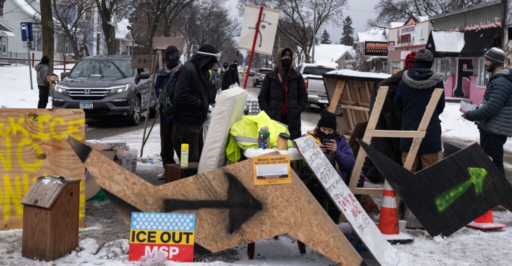 Anti-ICE protesters stand behind a makeshift barrier blocking a Minneapolis street.
