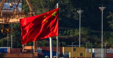CHONGQING, CHINA - AUGUST 12: The national flag of China waves in the wind at a container terminal on the Yangtze River, with dockside cranes and stacked shipping containers visible in the background, on August 12, 2025 in Chongqing, China. (Photo by Cheng Xin/Getty Images)