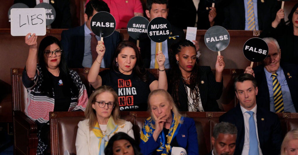 Democrat members of congress hold up signs and look on in anger during President Trump's 2025 address to Congress.