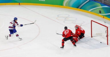 Team USA's Jack Hughes scoring winning goal against Canada, with puck going past goalie.