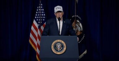 President Donald Trump behind a podium, in blue jacket, white shirt and 