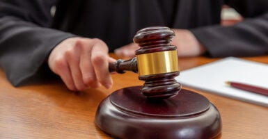 Female hand holding an auction law gavel. Woman judge with a notepad beating a wooden mallet, close up view.