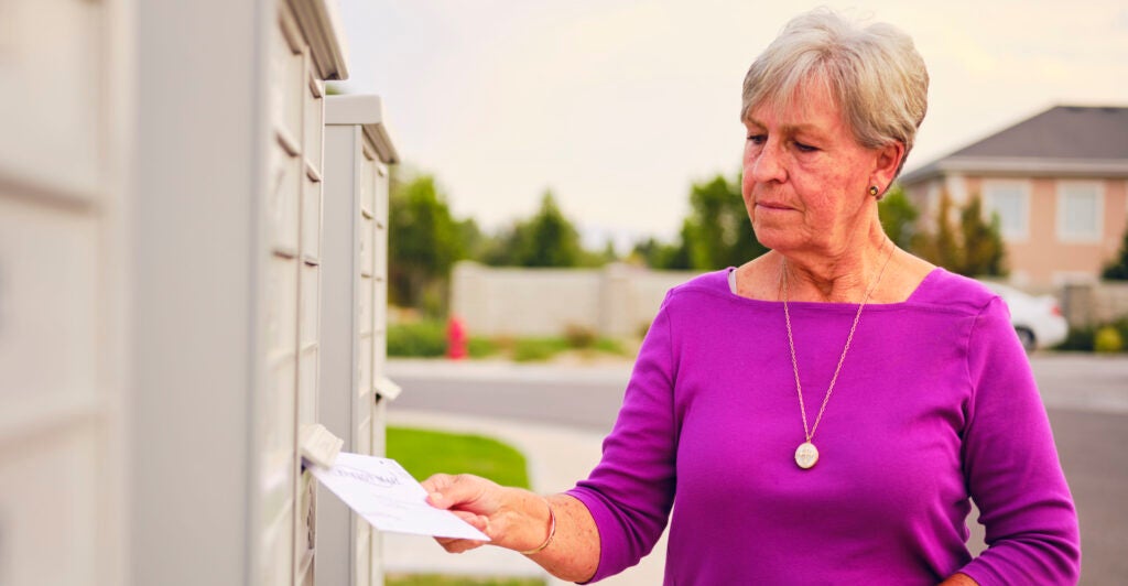 A senior age woman putting her vote by mail ballot into a mailbox.