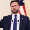 Vice President JD Vance gestures while he stands at a podium with American flags in the background.
