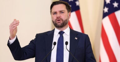 Vice President JD Vance gestures while he stands at a podium with American flags in the background.