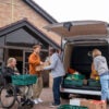 Volunteers unloading a van filled with food in trays for a food bank. They are in the North East of England. They are working together, passing the food back and forth.