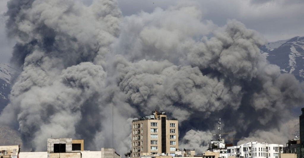 Huge dark plus of smoke rise above a row of buildings.