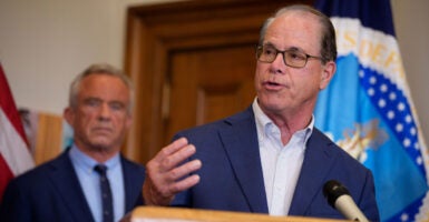 Indiana Gov. Mike Braun gestures while speaking at a podium, HHS Secretary Robert F. Kennedy Jr. behind him.