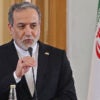 Iranian Foreign Minister Abbas Araghchi holds a microphone at a podium with the Iranian flag behind him.