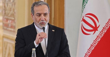 Iranian Foreign Minister Abbas Araghchi holds a microphone at a podium with the Iranian flag behind him.
