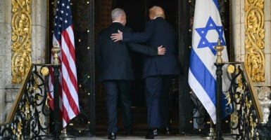 Benjamin Netanyahu and Donald Trump walk with arms on each other's back into doorway flanked by American and Israeli flags.