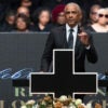 Barack Obama with his index finger on left hand pointing upward speaks behind a black cross at the funeral of Jesse Jackson.
