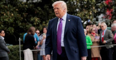 President Donald Trump walking. In background, a lined-off group of spectators.