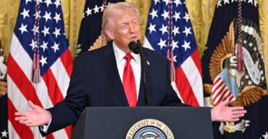 Donald Trump in front of a row of flags with his arms outstretched wide.