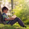 Boy sitting large tree reading.