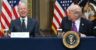 A laughing Energy Secretary Chris Wright being addressed by President Donald Trump as they sit at a long table.