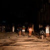 Cuban citizens on dark street lit only by car headlights amid blackout.