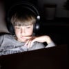 Boy in shirt reading "No Limits, No Rules" in a dark room, his face lit by a computer screen.