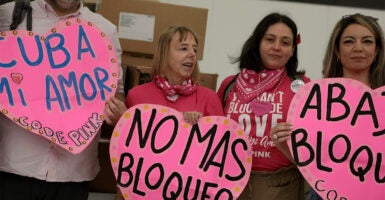 MIAMI, FLORIDA - MARCH 20: (L-R) Medea Benjamin, Jazmin Rumbaut,and Michelle Ellner from CODEPINK hold signs as they check in boxes of humanitarian aid at Invicta Air Charter in the Miami International Airport on March 20, 2026 in Miami, Florida.