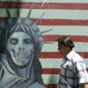 TEHRAN, IRAN: An Iranian couple walk past an anti-US mural painting outside the former United States' embassy in Tehran, 07 June 2005. Iranian voters are more accustomed to hearing their politicians chant "Death to America" -- but ahead of next week's presidential election the issue of relations with the US has been turned on its head. It is an ironic shift for the Islamic republic, founded on the dogma of resisting "Zionist-American conspiracies" and priding itself on standing up to the "Great Satan". AFP PHOTO/ATTA KENARE (Photo credit should read ATTA KENARE/AFP via Getty Images)