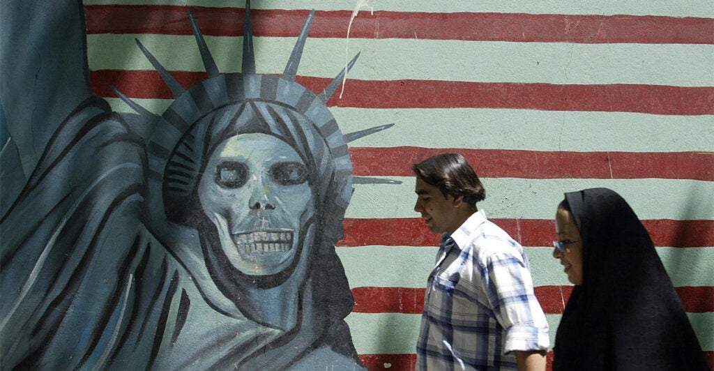 TEHRAN, IRAN: An Iranian couple walk past an anti-US mural painting outside the former United States' embassy in Tehran, 07 June 2005. Iranian voters are more accustomed to hearing their politicians chant "Death to America" -- but ahead of next week's presidential election the issue of relations with the US has been turned on its head. It is an ironic shift for the Islamic republic, founded on the dogma of resisting "Zionist-American conspiracies" and priding itself on standing up to the "Great Satan". AFP PHOTO/ATTA KENARE (Photo credit should read ATTA KENARE/AFP via Getty Images)