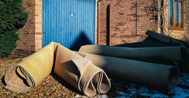 Four or five rolled up carpet pieces outside a brick building.