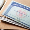 A Social Security card lays atop brown folders next to a calculator.