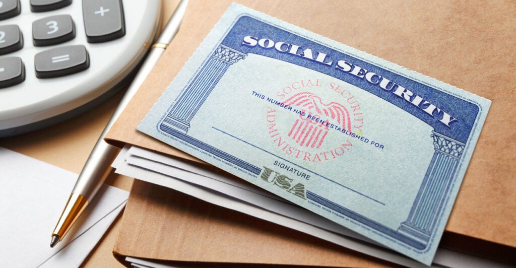 A Social Security card lays atop brown folders next to a calculator.