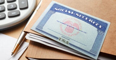 A Social Security card lays atop brown folders next to a calculator.