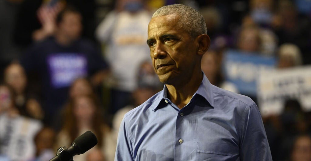 Barack Obama in a blue shirt looking stern.