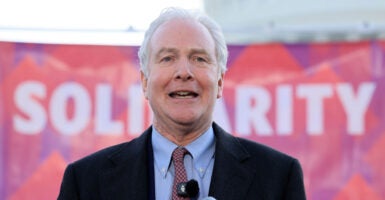 Sen. Chris Van Hollen, D-Md., speaks in front of a pink sign reading 