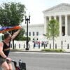 A man waves a rainbow flag as he rides by the Supreme Court on a bike.