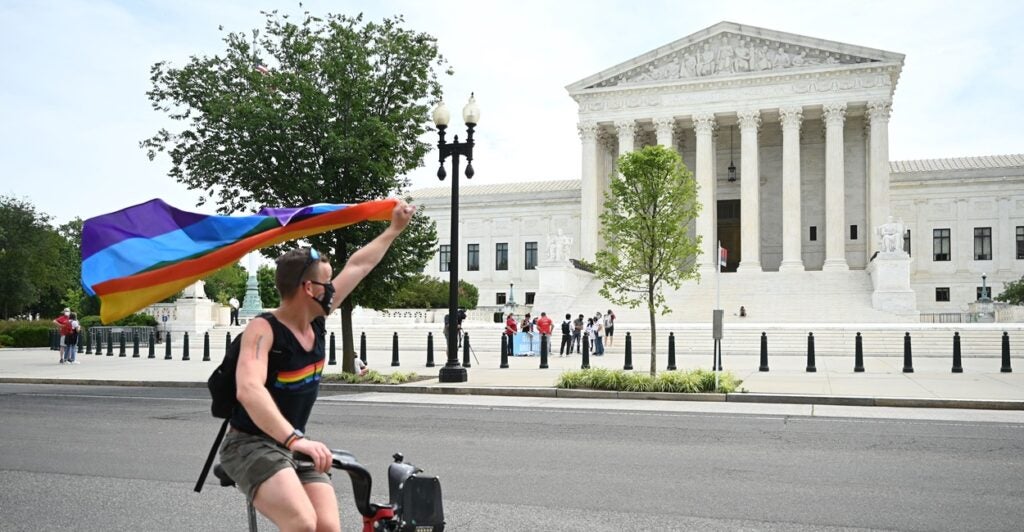 A man waves a rainbow flag as he rides by the Supreme Court on a bike.