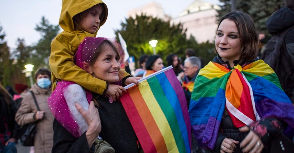 One adult woman and two female children holding rainbow flags.