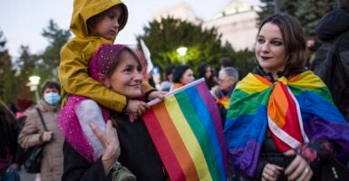 One adult woman and two female children holding rainbow flags.