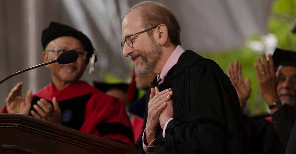 Man in academic robes with his hands against his heart standing at a podium.