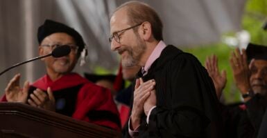 Man in academic robes with his hands against his heart standing at a podium.