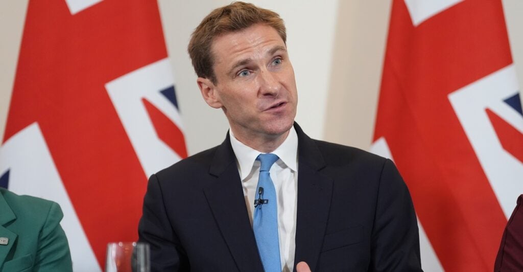 A man speaking in front of British flags.