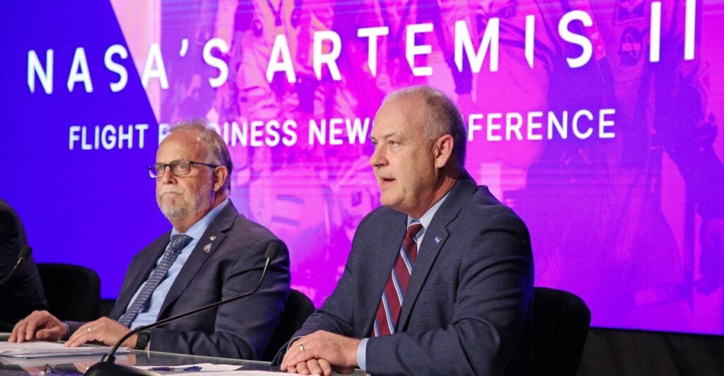 Two men sitting at a table in front of the words "Artemis II."