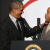 President Barack Obama greets Rev. Al Sharpton on a podium.