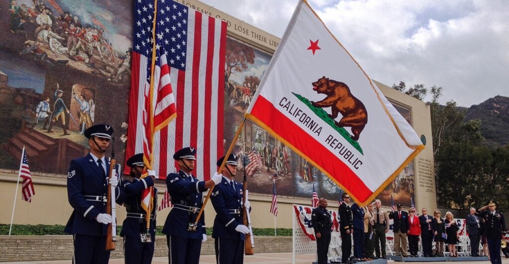 Uniformed men at a Veterans Day observance with a California flag.