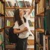 Female student reaching up for a book in a school library stack.