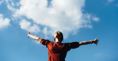 Woman outside in red shirt with her arms outstretched.