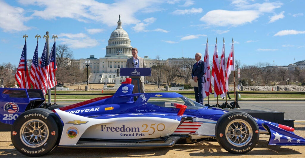 Race car driver and IndyCar Series champion Josef Newgarden speaks at the press conference for the Freedom 250 Grand Prix of Washington DC on the National Mall on March 09, 2026 in Washington, DC. In the foreground, a red, white and blue racecar.