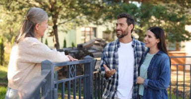 Friendly relationship with neighbors. Happy young couple talking to senior woman near fence outdoors.