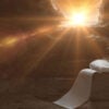 Artistic rendering of Jesus's empty tomb, with his burial shroud laying on stone and a burst of sunlight through the entrance.