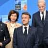 French President Emmanuel Macron stands in the center of a group of NATO leaders in front of blue NATO background.