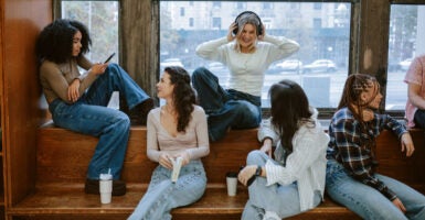 A mixed-raced group of young women sit on a bench and ledge interacting.